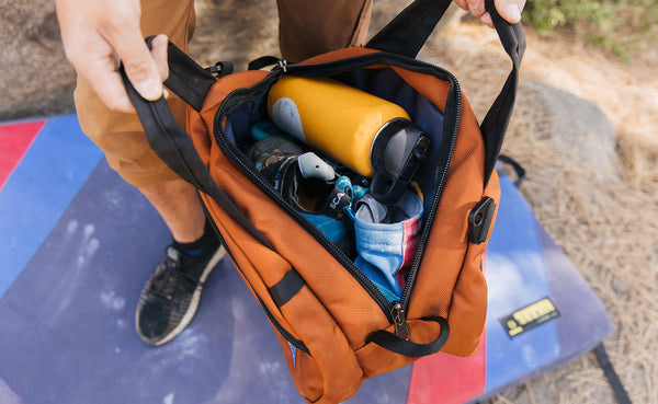 A person holding the Old-School Carry All open: you can see inside of the main compartment and it's packed with a water bottle, chalk bag and other items.
